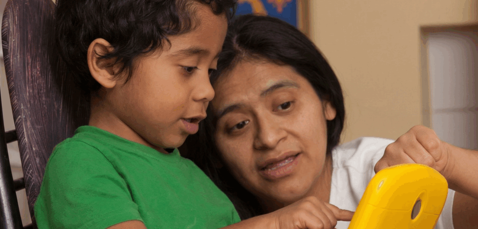 hispanic mother and young son looking at toy laptop